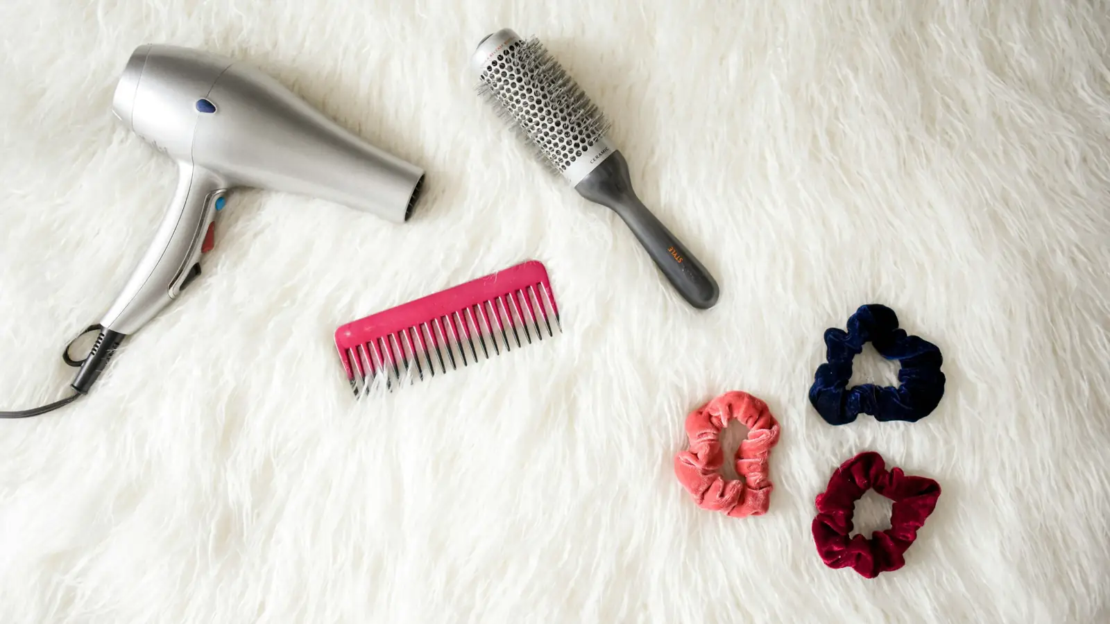 Secador de cabelo, escova, pente e elásticos sobre tapete branco
