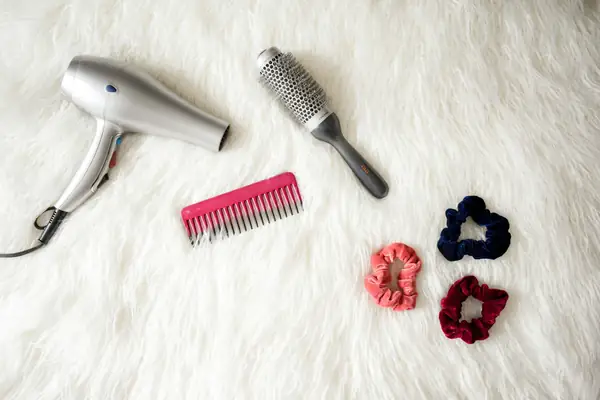 Secador de cabelo, escova, pente e elásticos sobre tapete branco