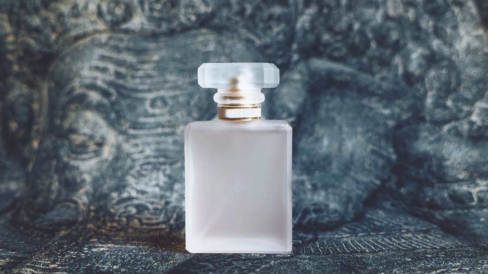 Frasco de perfume fosco sem marca sobre fundo de pedra esculpida