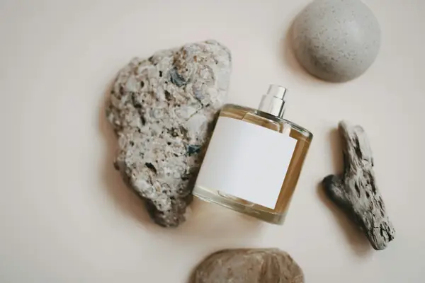 Frasco de perfume sem marca apoiado entre pedras sobre fundo claro