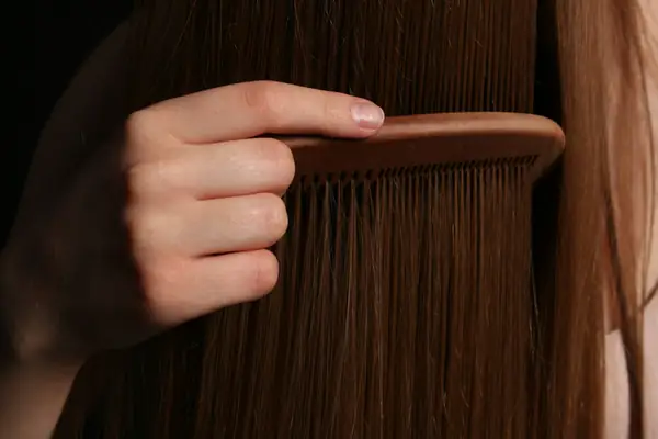 Mão penteando cabelo castanho longo com pente de madeira