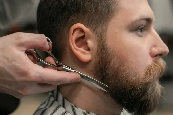 Barbeiro aparando a barba de um cliente com tesoura